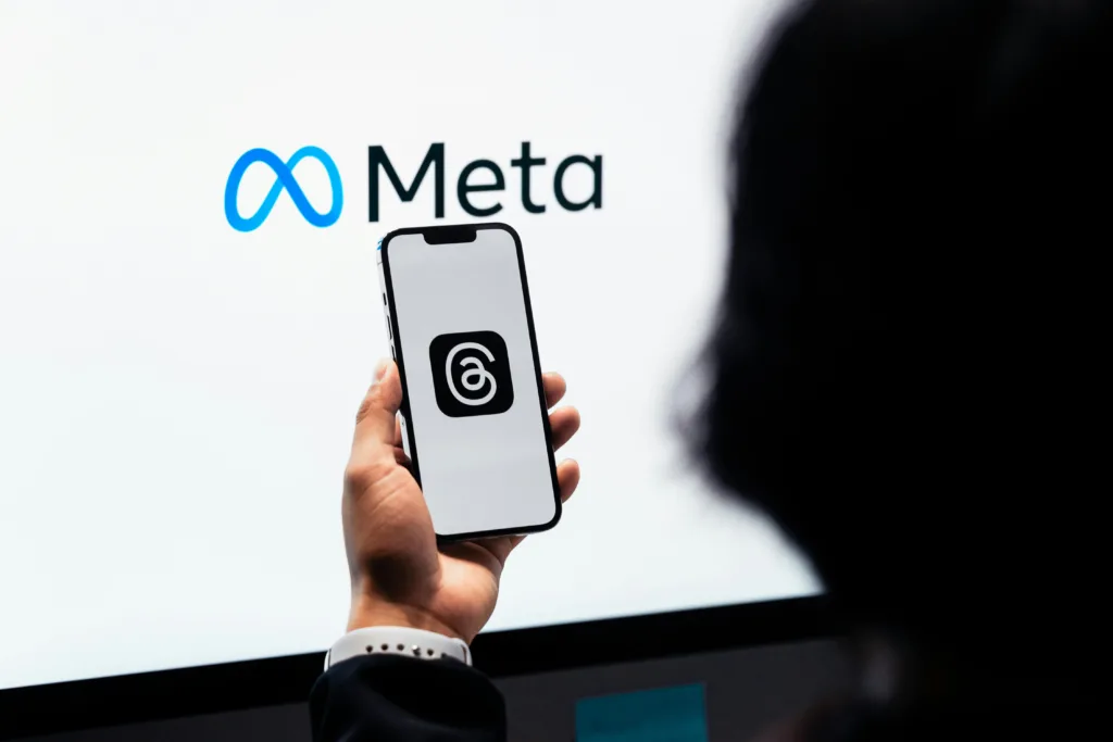 an image of woman holding a phone with the logo on threads on it on a background of meta logo